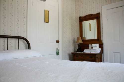 Cozy bedroom with a bed, vintage mirror, lamp, and a wooden dresser against floral wallpaper.