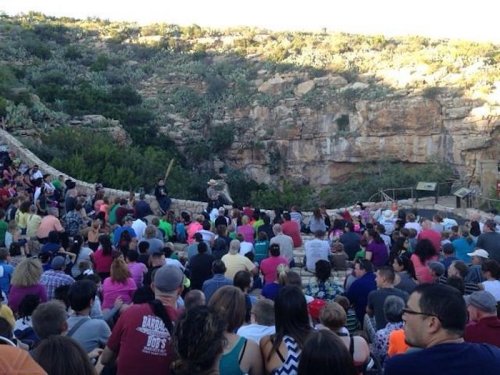 A large crowd gathers in an outdoor amphitheater surrounded by rocky terrain, enjoying a performance or event.