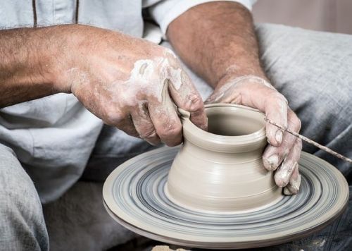A potter shaping a clay vessel on a spinning wheel, hands covered in clay.