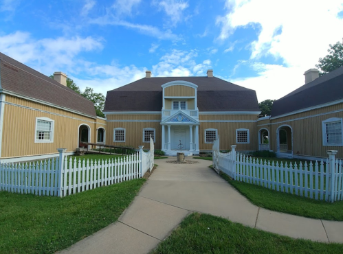 A large yellow house with white trim, surrounded by a white picket fence and green grass under a blue sky.