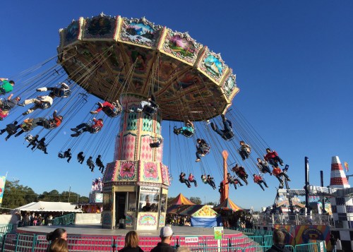 A colorful swing ride at a fair, with people enjoying the ride against a clear blue sky.
