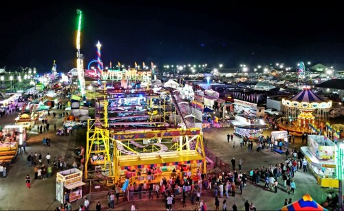 A vibrant night scene of a carnival with rides, games, and colorful lights, bustling with crowds.