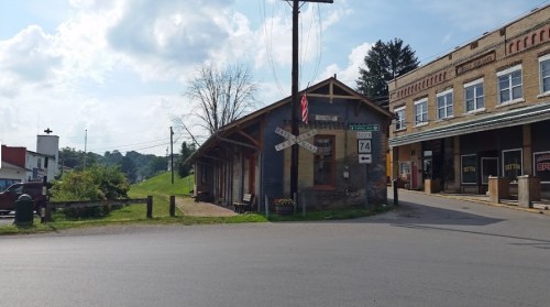 A small town intersection featuring a rustic building and a sign for Route 74, with greenery in the background.