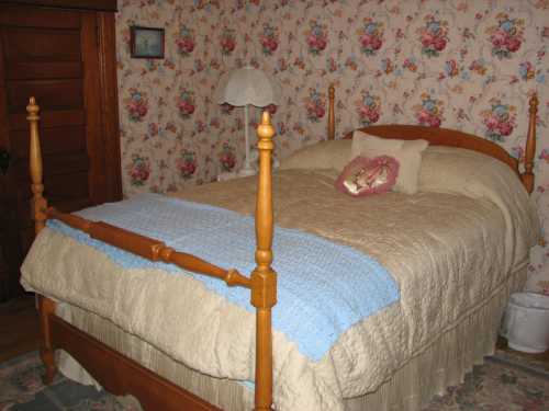 A cozy bedroom featuring a floral wallpaper, a wooden bed with a light quilt, and a bedside lamp.