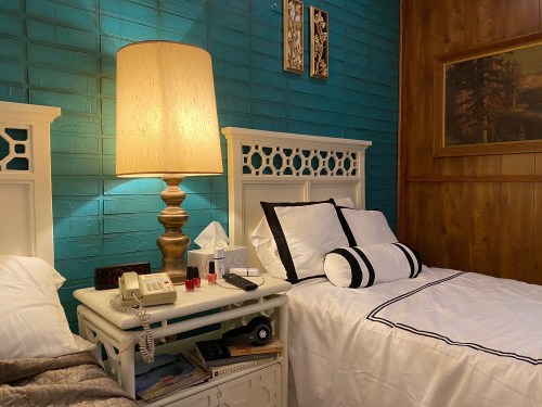 Cozy bedroom with two beds, a large lamp, and a nightstand featuring a phone and decorative items.