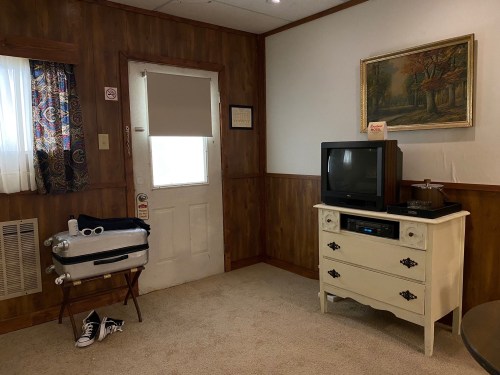Cozy room with wooden walls, a vintage TV, a dresser, and a door leading outside, featuring a small bathtub and a shoe.