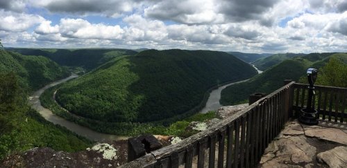 Panoramic view of lush green mountains and a winding river under a cloudy sky from a scenic overlook.