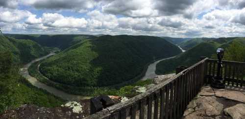 Panoramic view of lush green mountains and a winding river under a cloudy sky from a scenic overlook.