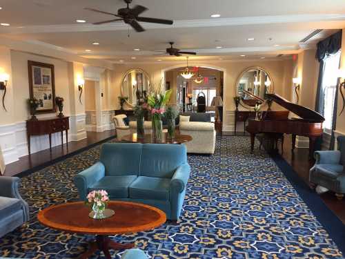 A spacious, elegantly decorated lobby with blue seating, a grand piano, and floral arrangements.