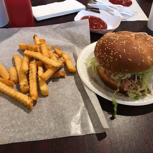 A plate with a sesame seed burger topped with lettuce and a side of golden French fries. Ketchup packets are nearby.