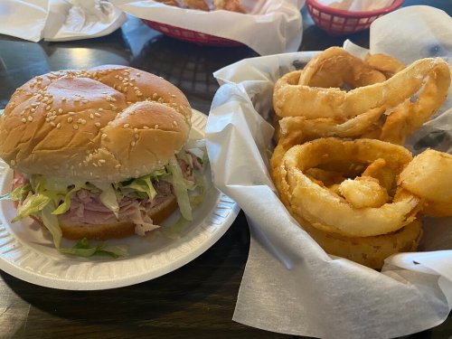A sesame seed bun sandwich with lettuce and ham, alongside a basket of crispy onion rings.
