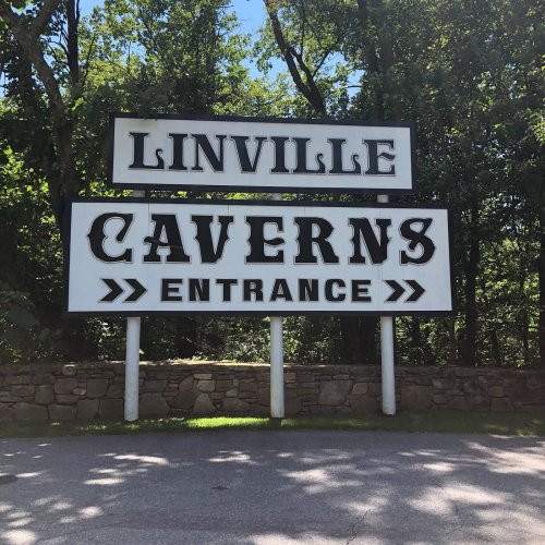 Sign for Linville Caverns with "Entrance" below, surrounded by trees and a clear blue sky.