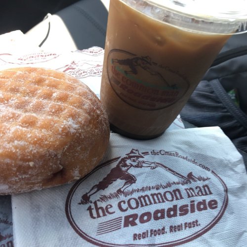 A donut and iced coffee on a napkin from "The Common Man Roadside," set in a car.