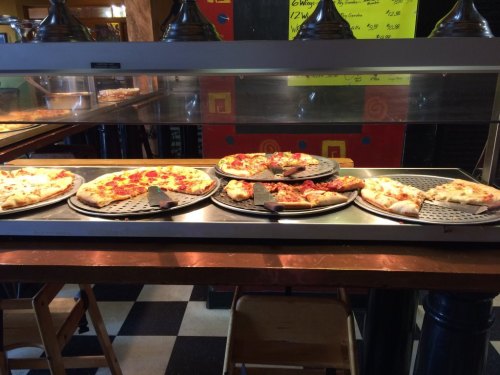 A display of various pizzas on a counter, with different toppings and slices ready to serve.