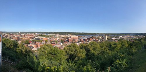 Panoramic view of a city skyline surrounded by greenery under a clear blue sky.