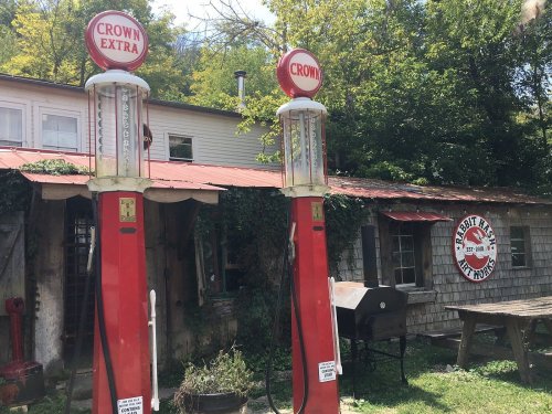 Two vintage gas pumps in front of a rustic building with a red roof and ivy-covered walls.