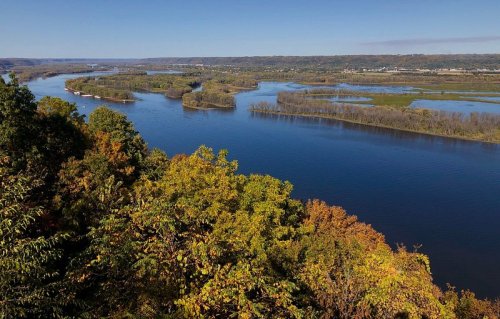 A scenic view of a river winding through lush green and autumn-colored trees under a clear blue sky.
