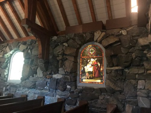 Interior of a stone church featuring stained glass windows and wooden beams.