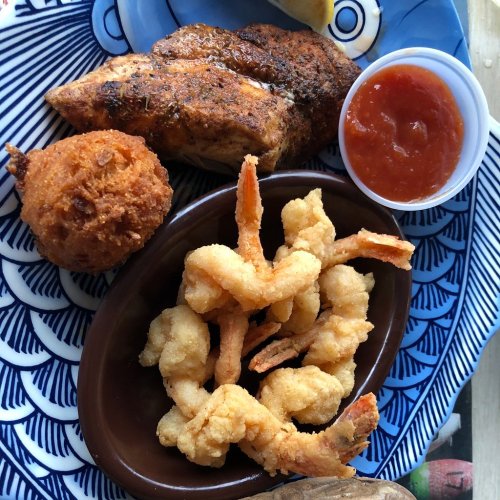 A plate featuring seasoned fish, fried shrimp, a hushpuppy, and a side of dipping sauce.