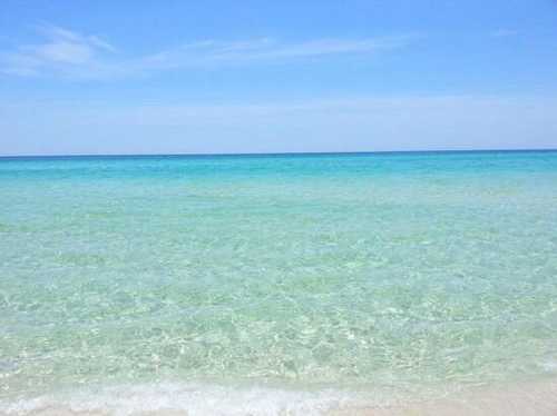 A serene beach scene with clear turquoise water and a bright blue sky. Gentle waves lap at the sandy shore.