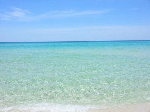 A serene beach scene with clear turquoise water and a bright blue sky. Gentle waves lap at the sandy shore.