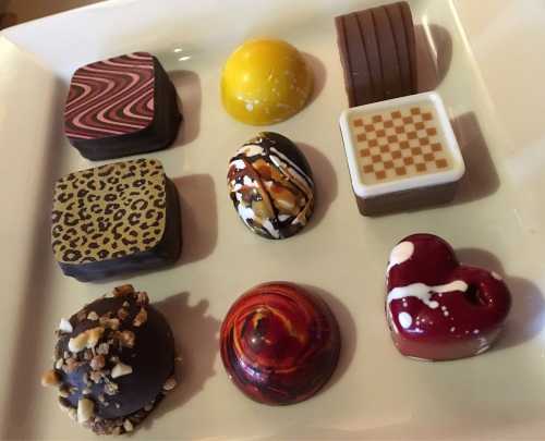 A plate of assorted chocolates in various shapes, colors, and patterns, including a heart and a checkered design.