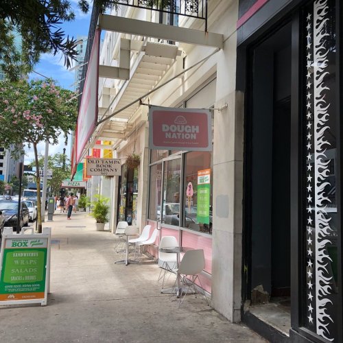 A street view featuring a shopfront with "Dough Nation" signage and outdoor seating, surrounded by greenery.
