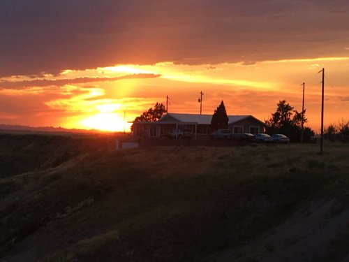 A sunset casts vibrant colors over a house and landscape, with power lines silhouetted against the sky.