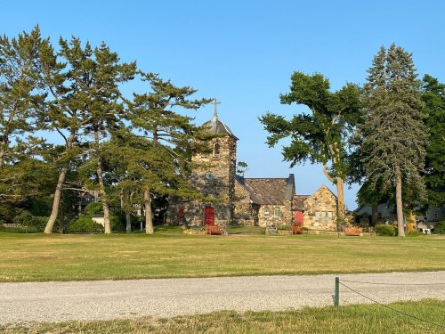 A stone building with a tower surrounded by trees and a grassy area, under a clear blue sky.
