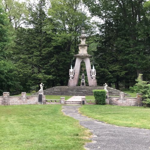A stone monument surrounded by trees, featuring statues and a landscaped pathway leading to it.