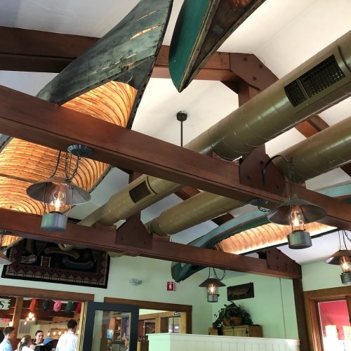 Interior of a restaurant featuring wooden beams, hanging canoe decor, and pendant lights.