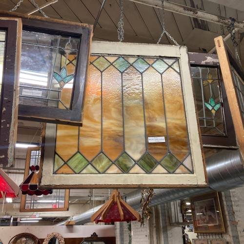 Stained glass window with geometric patterns, hanging among other vintage frames in a shop.