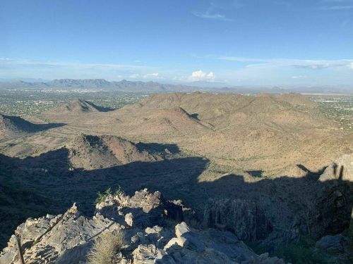 A panoramic view of rugged mountains and valleys under a clear blue sky, with distant peaks on the horizon.