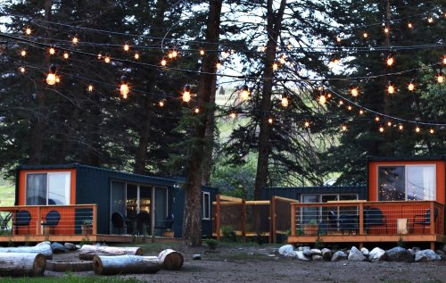 Cozy cabins surrounded by trees, with string lights overhead and logs arranged in a circle on the ground.