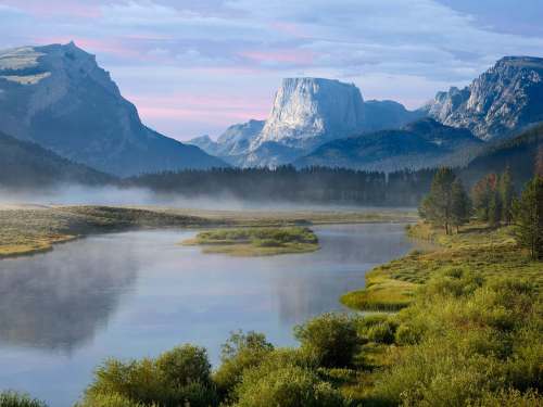 A serene landscape featuring a river, lush greenery, and majestic mountains under a soft, cloudy sky.