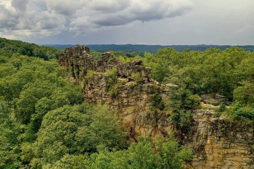A rocky outcrop surrounded by lush green trees under a cloudy sky, showcasing a scenic natural landscape.