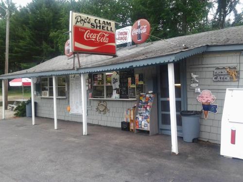 A small seafood restaurant with a sign reading "Pop's Clam Shell," featuring a menu board and outdoor seating.