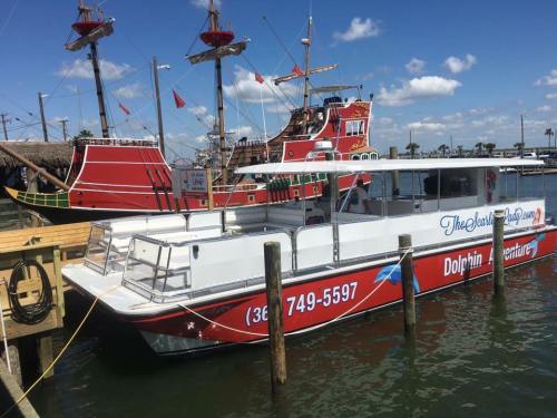 A white boat with red accents docked next to a large, colorful pirate ship under a blue sky.