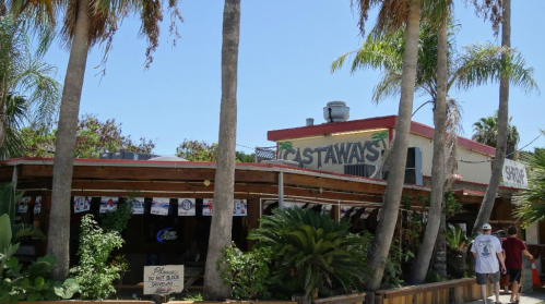 A tropical restaurant named "Castaways" surrounded by palm trees and greenery on a sunny day.