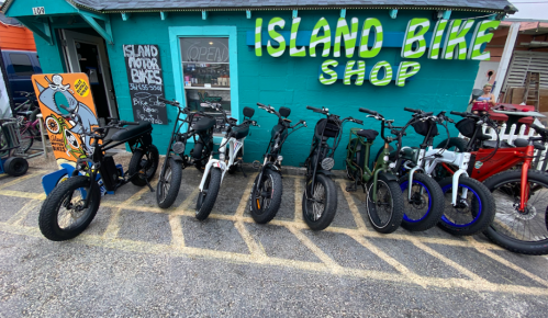 A row of various bicycles parked outside the colorful Island Bike Shop with a vibrant sign.