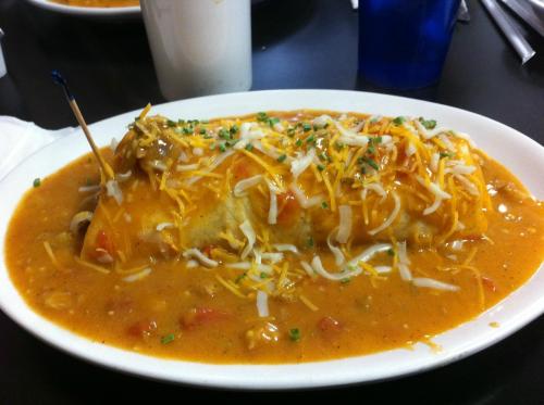 A plate of a smothered burrito topped with cheese, sauce, and garnished with green onions.