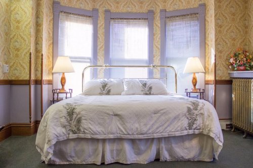 Cozy bedroom with a brass bed, floral bedding, and large windows, featuring lamps and vintage decor.
