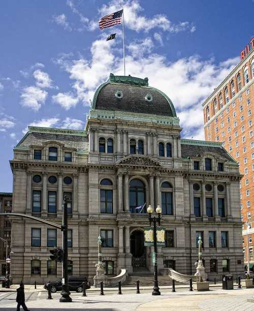Historic building with a green domed roof, American flag, and ornate architecture against a blue sky.