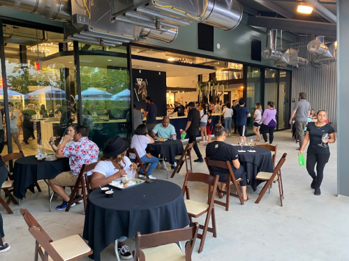 A bustling outdoor dining area with people eating at tables and a lively atmosphere in a modern restaurant setting.