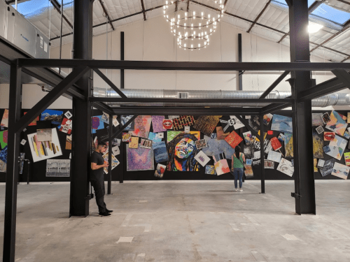 A spacious gallery with a black wall covered in colorful artwork and posters, featuring two people observing the display.