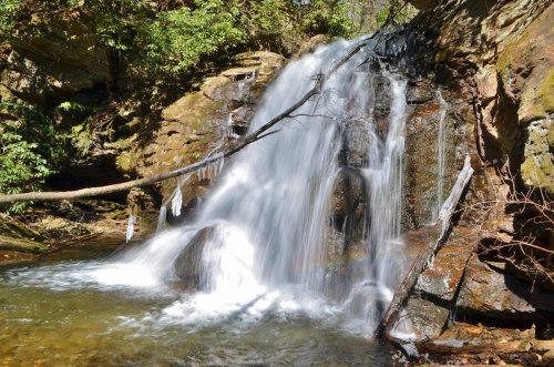 A serene waterfall cascading over rocks, surrounded by lush greenery and a clear pool of water below.