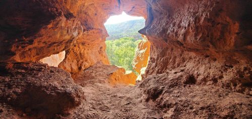 View from inside a cave, looking out at a bright landscape with greenery and rocky formations.
