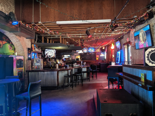 A dimly lit bar with colorful lights, arcade games, and a long counter with stools, creating a lively atmosphere.