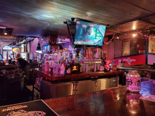 A lively bar scene with colorful lights, a large TV showing a movie, and a well-stocked bar counter.