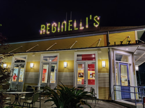 Exterior of Reginelli's Pizza at night, featuring bright signage and a welcoming entrance with outdoor seating.